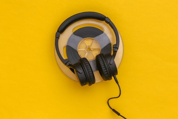 Stereo headphones and magnetic audio reel on yellow background. Top view