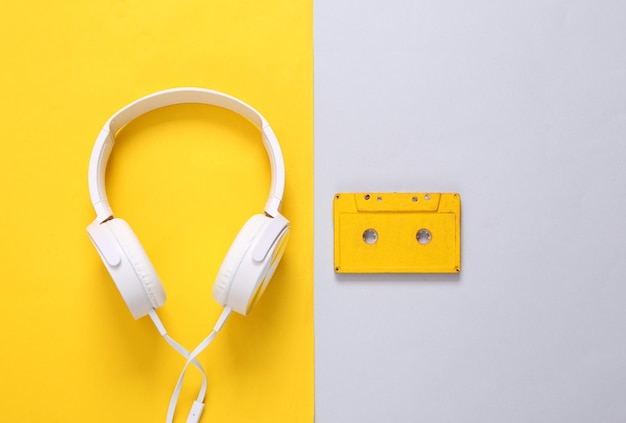 Stereo headphones with audio cassette on gray yellow background Retro 80s still life Top view