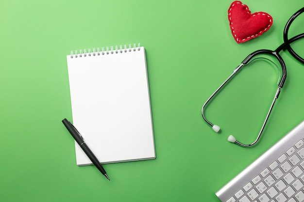 Photo stethoscope in doctors desk with notebook, keyboard and heart