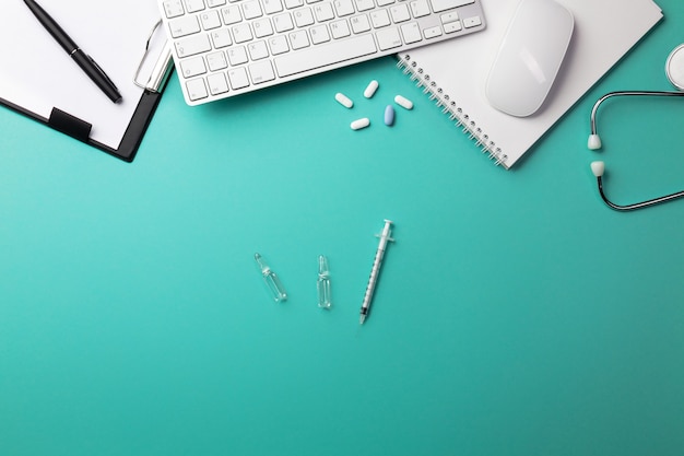 Stethoscope in doctors desk with notebook, pen, keyboard, mouse and pills