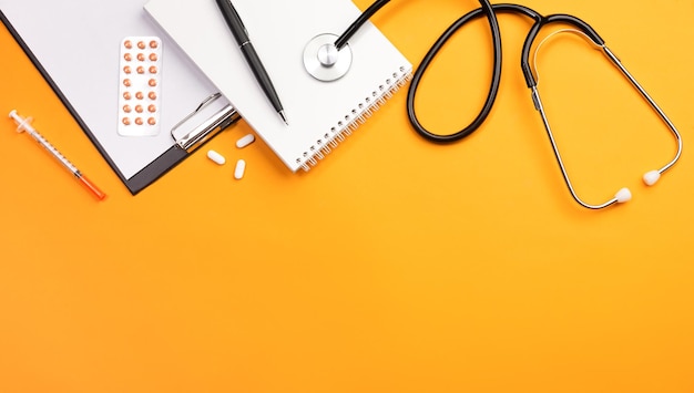 Stethoscope in doctors desk with notebook and pills top view