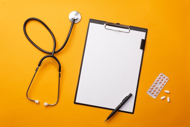 Stethoscope in doctors desk with tablet, pen and pills. Top view with place for your text.