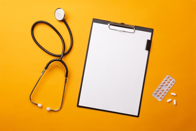 Stethoscope in doctors desk with tablet, pen and pills. Top view with place for your text.