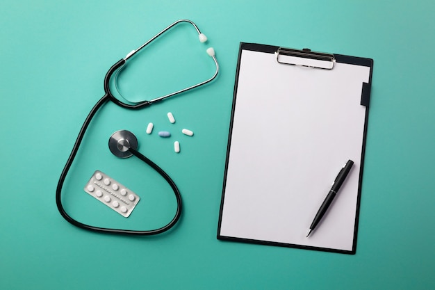 Photo stethoscope in doctors desk with tablet, pen and pills