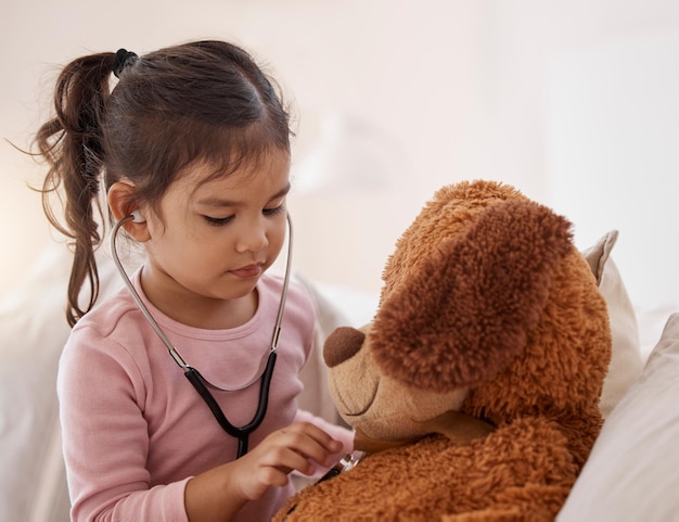 Stethoscope girl and a teddy bear playing future doctor game showing care on a good health insurance checkup Cute small child listening or checking stuffed animal medical heartbeat at home