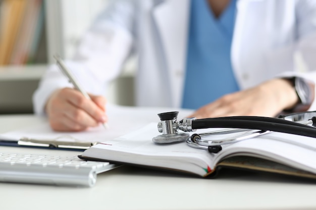 Stethoscope head lying on medical forms closeup while medicine doctor working in background.