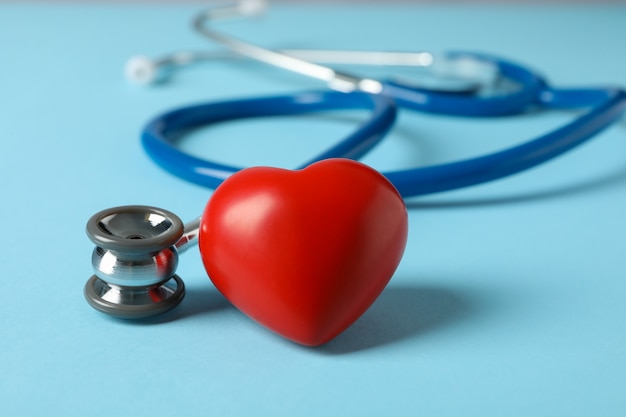 Stethoscope and heart on blue surface, close up