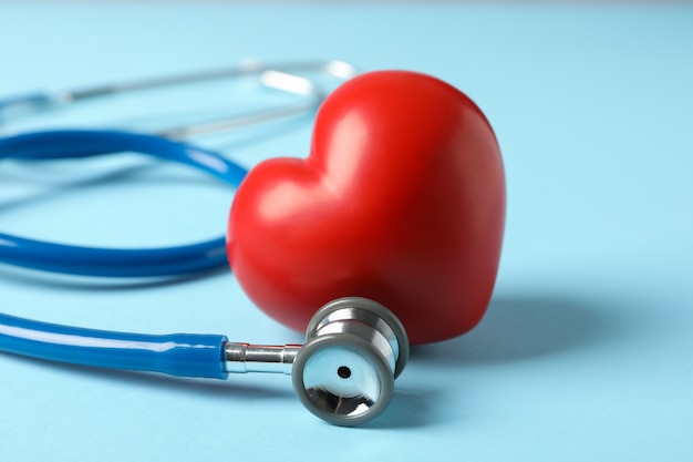 Stethoscope and heart on blue surface, close up