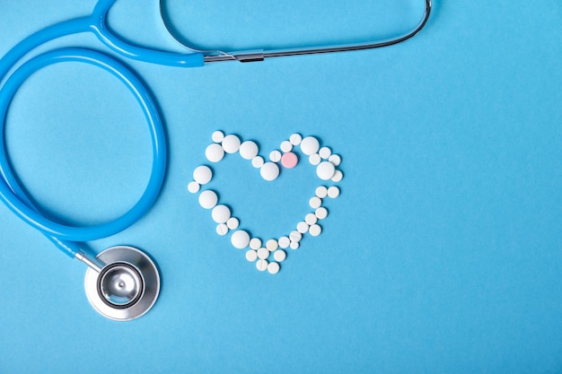 Stethoscope and heart from pills on blue background, cardiology concept