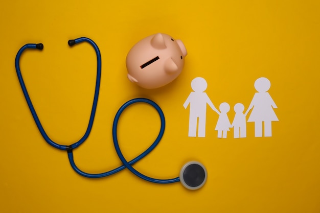 Stethoscope, paper chain family, piggy bank on yellow, health insurance concept