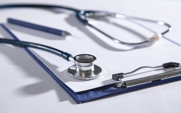 Stethoscope, pen, clipboard on white background.