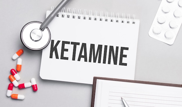 Stethoscope, pills and notebook with ketamine text on the medical table