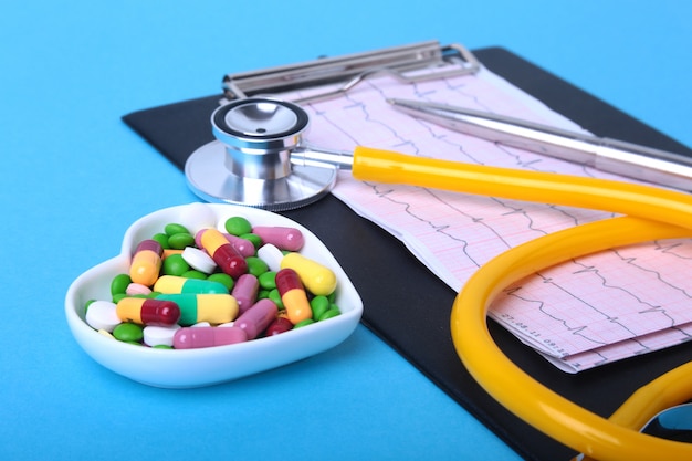 Stethoscope, prescription and colorful assortment pills and capsules on plate.