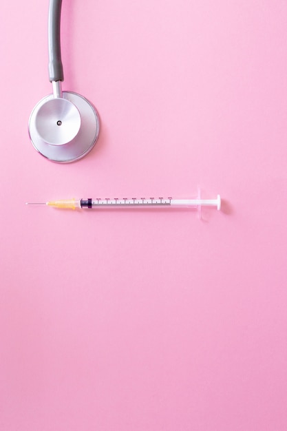 Stethoscope and syringe on pink table for coronavirus prevention.