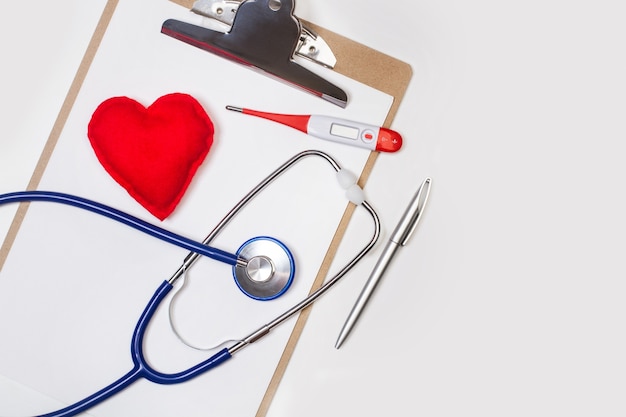 A stethoscope and a thermometer on a clipboard with a fabric red heart