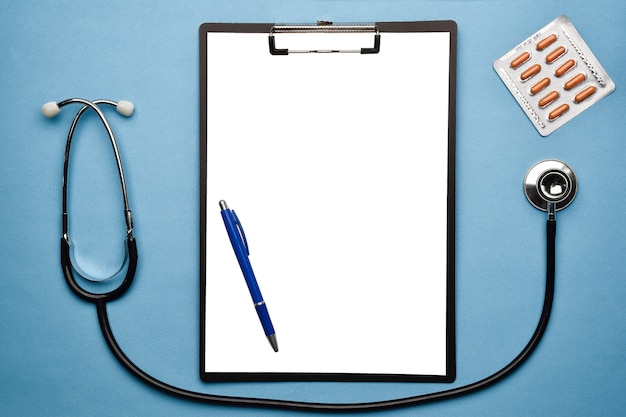 Stethoscope, whiteboard, pen and blister with pills lie on a blue background