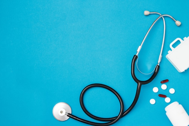 Stethoscope with pills on blue background. Health care concept. Top view, flat lay, copy space.