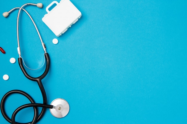 Stethoscope with pills on blue background. Health care concept. Top view, flat lay, copy space.