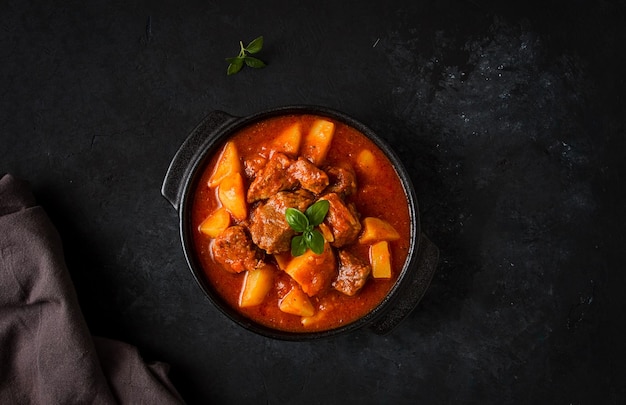 Stew with potatoes in tomato sauce with spices and herbs closeup no people on a black background