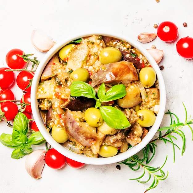 Stewed aubergines with vegetables and herbs in a bowl light background top view