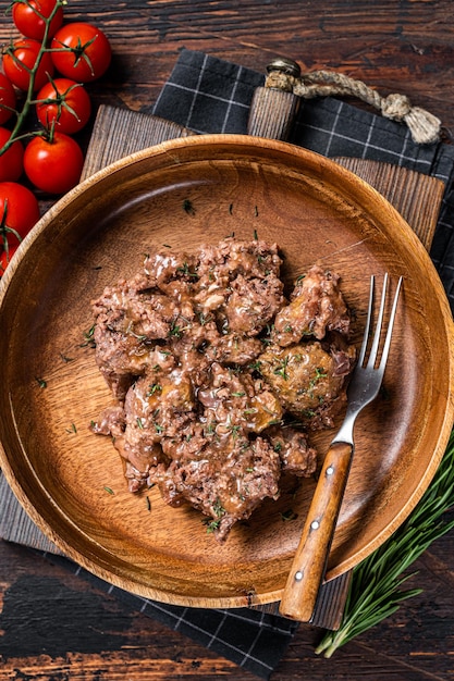 Stewed beef meat in a wooden plate Dark Wooden background Top view