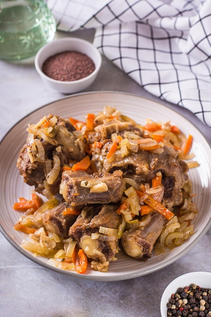 Stewed beef oxtail with wine and vegetables on a plate on the table vertical view