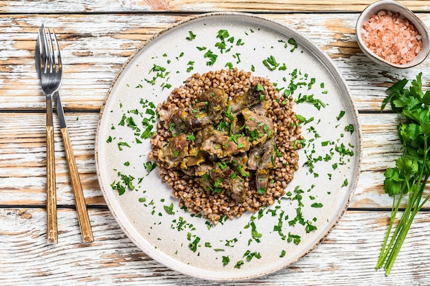 Photo stewed chicken stomachs with vegetables and buckwheat on a plate. wooden white background. top view.