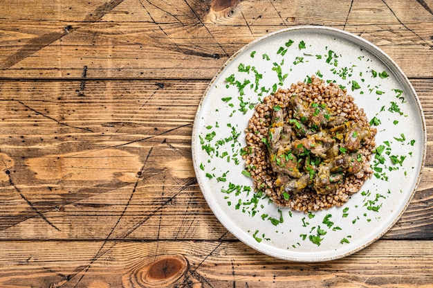 Photo stewed chicken stomachs with vegetables and buckwheat. wooden background. top view.