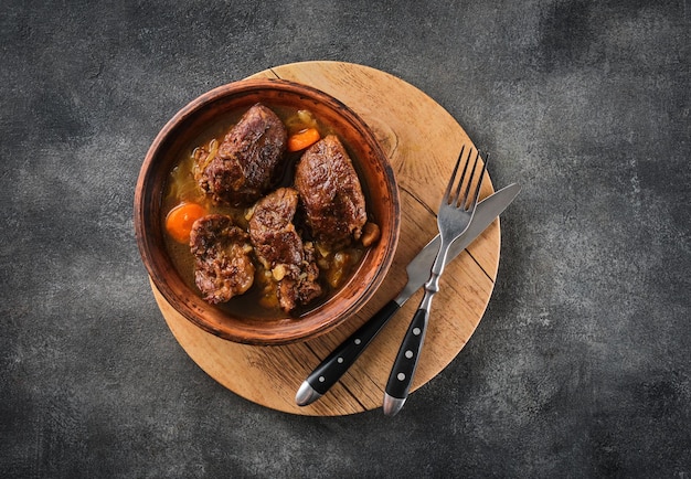 Stewed pork cheeks with vegetables with a grey background on an overhead shot Spanish or German food