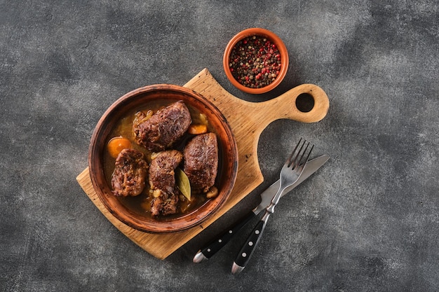 Stewed pork cheeks with vegetables with a grey background on an overhead shot Spanish or German food