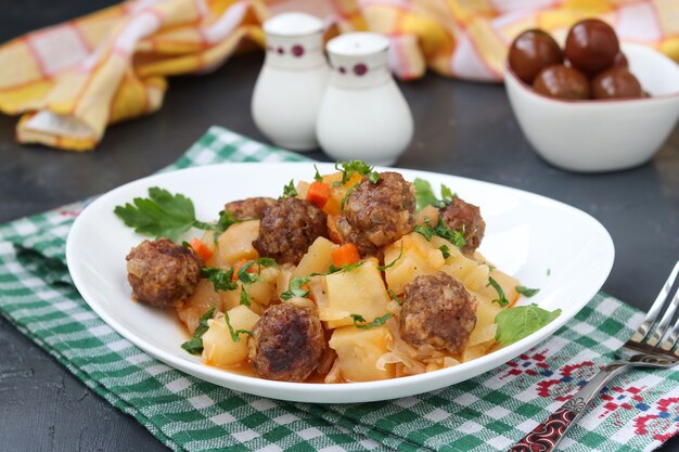 Stewed potatoes with meatballs on a white plate on dark