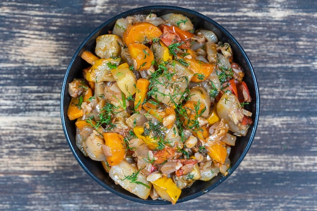 Photo stewed vegetables in a black bowl on wooden table