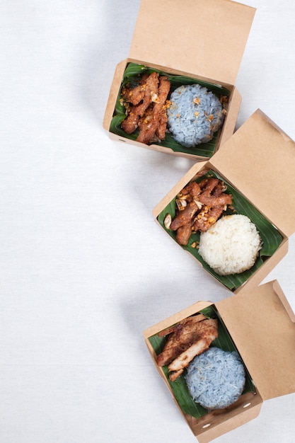 Sticky rice with grilled pork and fried pork put in a brown paper box, put on a white tablecloth, food box, Thai food.