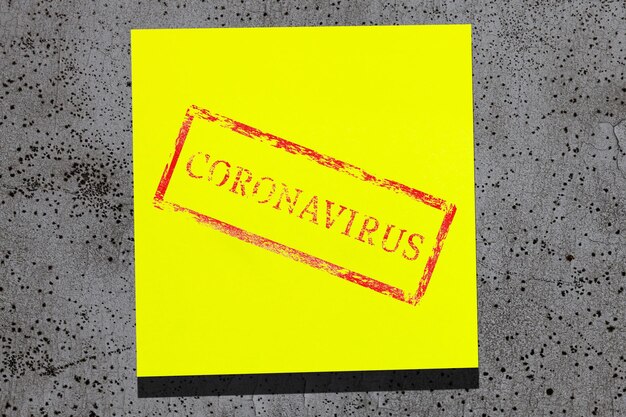 Photo sticky yellow sheet with coronavirus written on gray stone wall