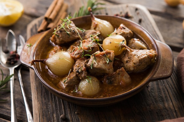 Stifado - delicious mediterranean beef stew with onion bulbs, cinnamon and spices in a casserole, on a black wooden table, view from above, close-up