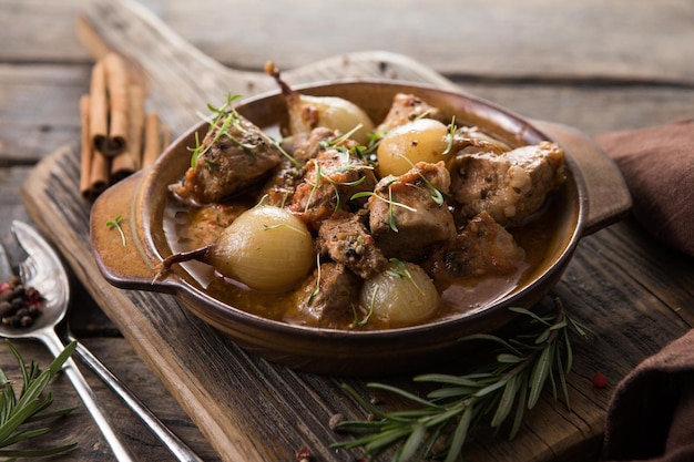 Stifado - delicious mediterranean beef stew with onion bulbs, cinnamon and spices in a casserole, on a black wooden table, view from above, close-up