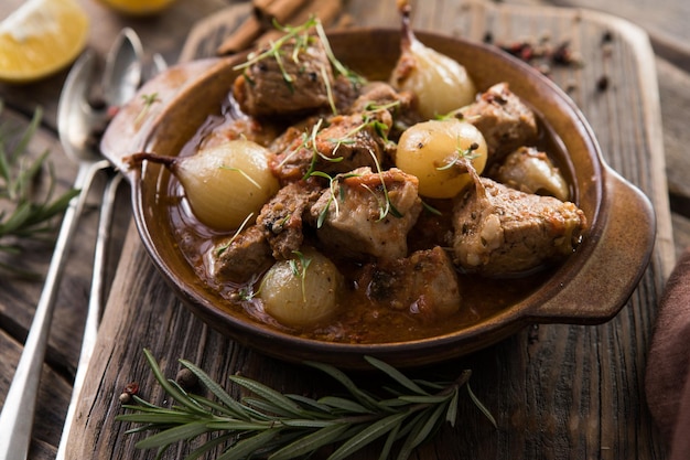 Stifado - delicious mediterranean beef stew with onion bulbs, cinnamon and spices in a casserole, on a black wooden table, view from above, close-up