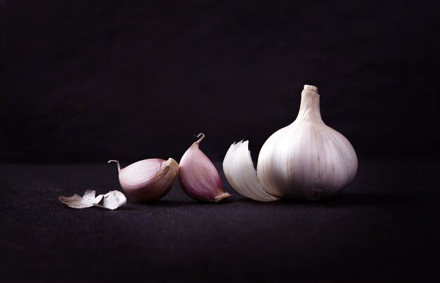  a still life arrangement of Three whole garlic bulbs grouped on black stone plate