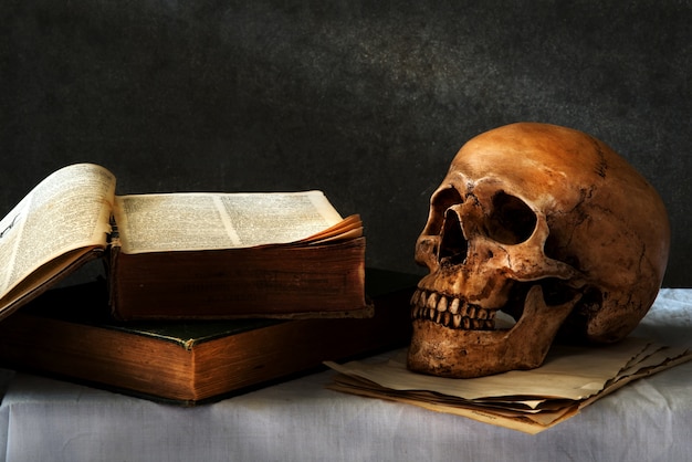 still life art photography on human skull skeleton with book omn desk