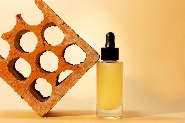 Still life of bottle with dropper of moisturizing cosmetic serum next to rustic red brick with writing space