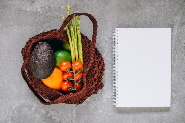 Still life of brown biodegradable shopping bag with raw vegetables on gray