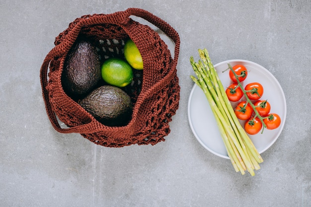 Still life of brown biodegradable shopping bag with raw vegetables on gray