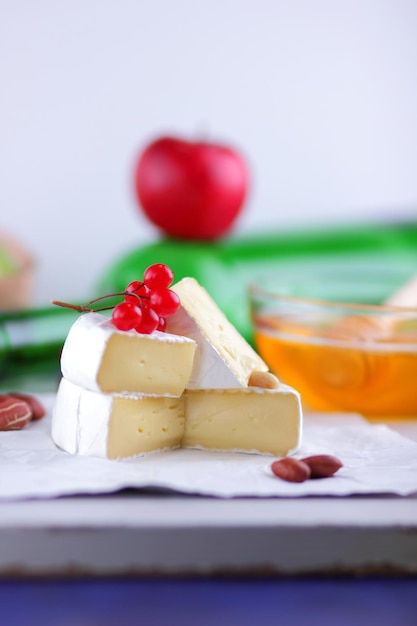 Still life of cheese fruit and a green bottle on a blurred background Camembert French cream cheese made from cow's milk served with honey and fruit on white parchment Closeup