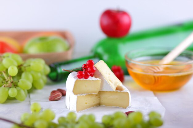 Still life of cheese fruit and a green bottle on a blurred background Camembert French cream cheese made from cow's milk served with honey and fruit on white parchment Closeup