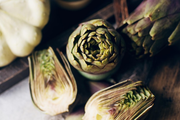 Still life composition with raw organic artichoke on vintage wooden board