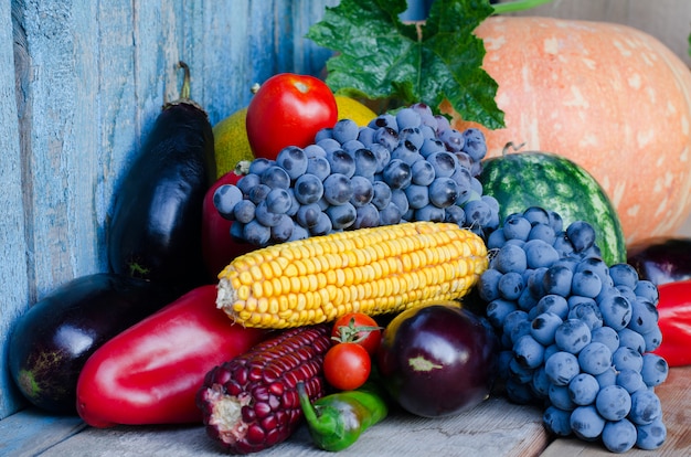 Still life of corn, grapes, eggplant, pumpkins and peppers on the old background.