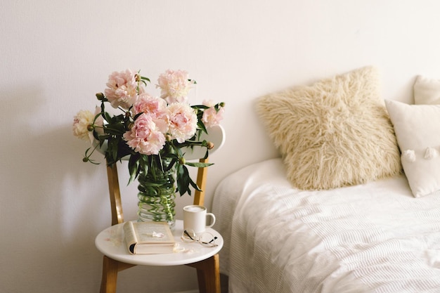 Still life details in home interior of living room Open book with glasses cup coffee and bouquet white pink peonies flowers Read and rest Cozy home