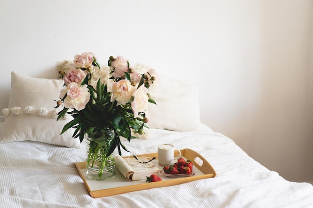 Still life details in home interior of living room Open book with glasses cup coffee strawberries and bouquet white pink peonies flowers Read and rest Cozy home