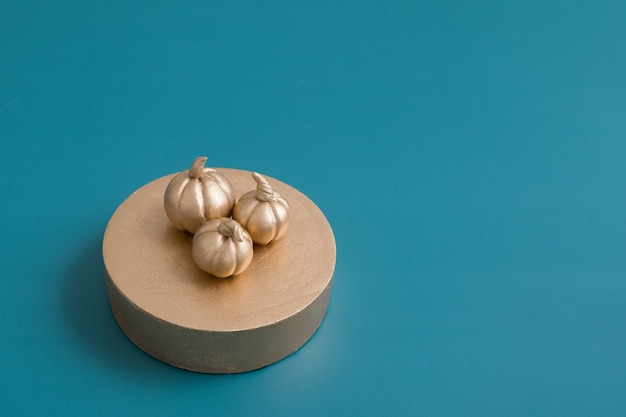 Still life of golden pumpkins on a podium on a turquoise background with copy space. Minimalistic concept of harvesting, autumn