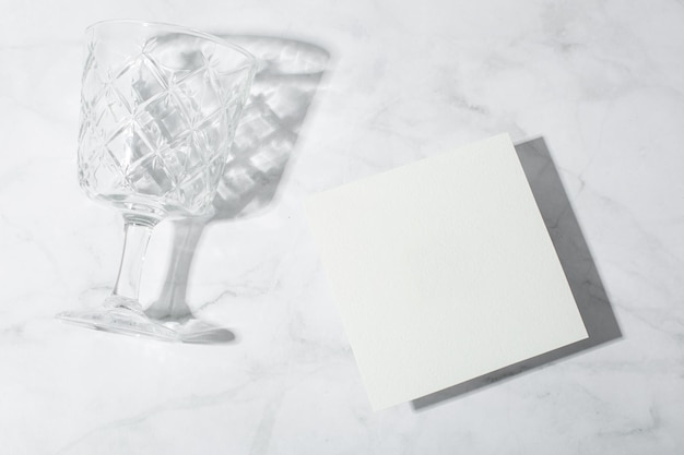 Still life scene with glasses on marble background in sunlight and blank business greeting card invi